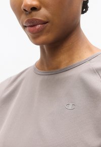 Γκρι κοντομάνικο πουκάμισο με υφασμάτινη υφή και στρογγυλή λαιμόκοψη, με ένα μικρό, διακριτικό λογότυπο στο μπροστινό μέρος.