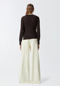 Maglione nero a coste con maniche lunghe, abbinato a pantaloni giallo pallido a gamba larga con tasche posteriori. Dettaglio di bottoni sul lato del maglione.