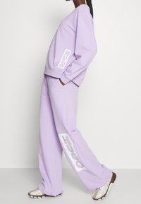 Persona negra vistiendo un sudadera oversized lila y pantalones a juego con acentos de logo en blanco, combinados con zapatillas chunky blancas y beige.