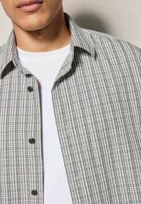 Skjorte med knapper i et blåt og hvidt ternet mønster, lavet af bomuldsstof, blød tekstur, med en spids krave og sorte knapper foran.