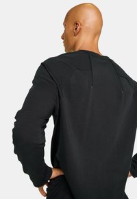 Svart långärmad t-shirt med rund halsringning, texturerad tyg, med detaljerad sömnad vid axlar och rygg, samt avslappnad passform.