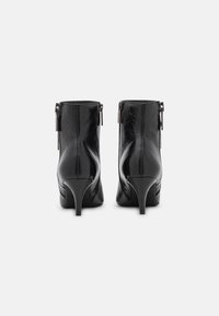 Par de botas de piel negras hasta el tobillo con cremalleras traseras y tacones cónicos de altura media sobre un fondo blanco.