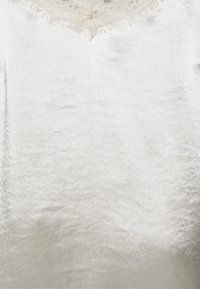 Silk top in light silver with a scalloped lace neckline. Smooth texture with slight sheen and fringe detailing at the collar.