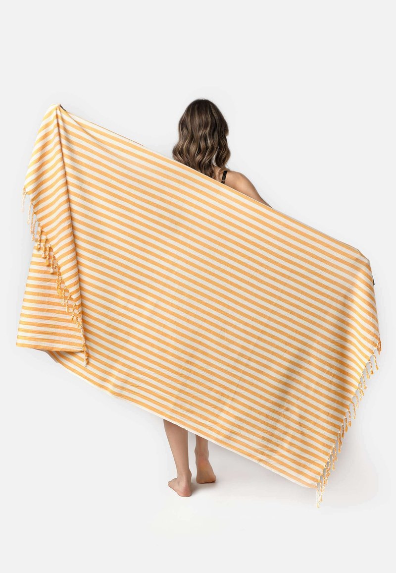 Couverture rayée jaune et crème, fabriquée en tissu doux. Présente des franges sur un bord et a une forme rectangulaire.
