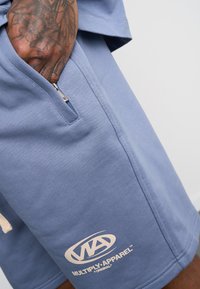 Light blue cotton shorts featuring a zip pocket and an embroidered logo in cream, with a soft texture and relaxed fit.