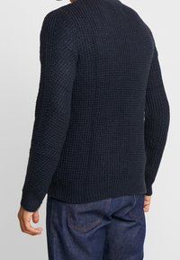 Marinblå stickad tröja med en texturerad väv, rund hals och långa ärmar. Ribbstickade mudd och fåll framhäver den åtsittande designen. Avslappnad stil.