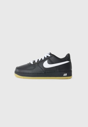 Melna ādas sporta apava ar baltu swoosh, ar šņorēm, gumijas zole ar dzeltenām akcentiem un "AIR" zīmola nosaukums uz papēža.