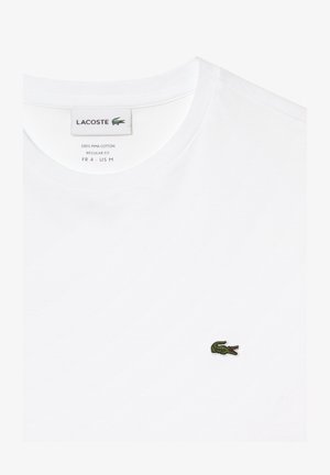 Vit T-shirt tillverkad av 100% Pima-bomull, med rund halsringning och en liten grön broderad krokodil-logotyp på vänster bröst.