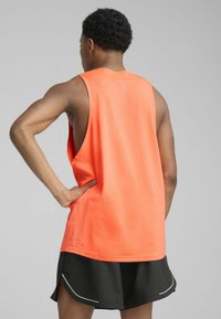 Orange ærmeløs atletisk tanktop med en afslappet pasform, der har en blød tekstur og en rund kant, parret med sorte shorts og hvide detaljer.