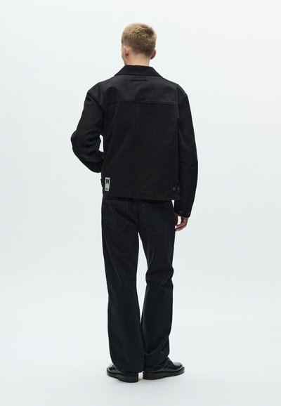 Μαύρο τζιν μπουφάν με γιακά, ορατές ραφές και διακοσμητικά κουμπιά. Συνδυασμένο με σκούρα τζιν με ίσια γραμμή και μαύρα παπούτσια.