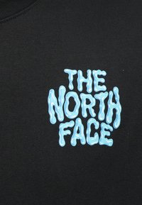 Μαύρο ύφασμα με κυματιστό, ανοιχτό μπλε κείμενο που γράφει "THE NORTH FACE" σε ένα στιλιζαρισμένο, «λιωμένο» γραμματοσειρά.