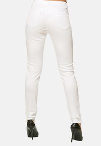 Jeans blancos ajustados con una textura suave y bolsillos traseros, combinados con tacones negros, que muestran una silueta ceñida.
