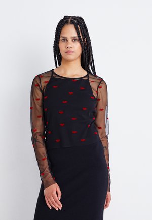 Top nero con maniche lunghe in mesh trasparente, caratterizzato da un motivo di labbra rosse. Collo rotondo e vestibilità comoda. Indossato con una gonna nera.