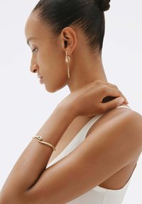 Pendientes de oro con un diseño de cadena en cascada y un acento en forma de hoja; pulsera de oro con un motivo de serpiente texturizado y un detalle de esmeralda.