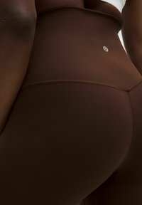 Leggings marron taille haute en tissu lisse et extensible, avec un détail de couture et un accent de logo à l'arrière.