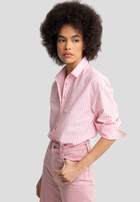 Camisa de botones a rayas rosa y blanca con cuello puntiagudo y mangas enrolladas, combinada con unos jeans de tiro alto rosa claro.