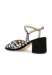 Musta mokkanahka korkeakorkoinen sandaali, jossa on paksu korko, ristiin menevät hihnat ja hopeiset pyramidi-nastat hihnoissa.