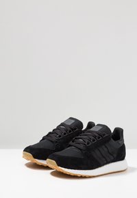 Mustat tennarit, joissa on mokkaa ja verkkomateriaalia, pyöreät nauhat sekä teksturoitu valkoinen keskipohja kuminahkaisella ulkopohjalla.