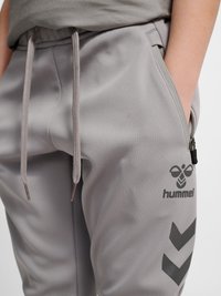 Close-up of gray sweatpants with drawstrings, a zippered side pocket, and black Hummel logo and chevron patterns on the thigh.