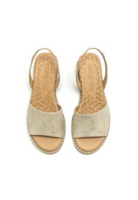 Sandales en suède beige avec une large lanière à l'avant et un dos ouvert. La semelle intérieure présente un motif de feuilles, et il y a des coutures décoratives le long de la semelle.