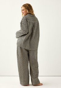 Czarny i kremowy w kratę zestaw piżamowy, zawierający koszulę z kołnierzykiem i długimi rękawami oraz luźne spodnie w dopasowanym wzorze.