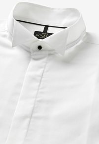 Camisa de cuello blanco hecha de 100% algodón, con un acabado texturizado, un cuello abotonado y un pequeño botón negro de acento en el cuello.
