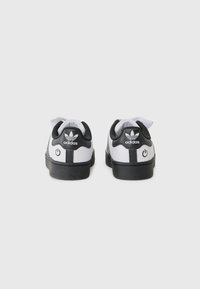 Baskets Adidas noir et blanc avec un dessus texturé, un bout rond et des accents de logo. Comprend une bande contrastante et un graphique de bouton sur le talon.