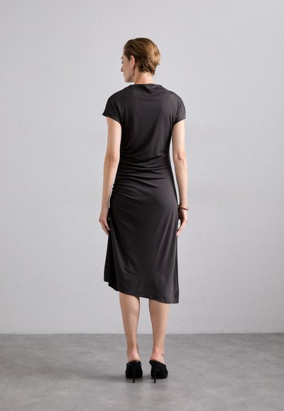 Black, knee-length dress made of soft, stretchy fabric. Features short sleeves and a gathered detail at the back. Worn with black heeled shoes.
