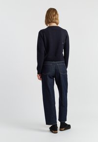 Maglione navy a maniche lunghe e scollo rotondo, abbinato a pantaloni in denim scuro a vita alta con vestibilità comoda e tasche posteriori.
