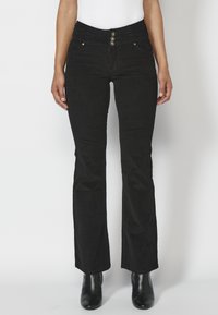 Jeans de campana negros con una cintura alta, que cuentan con tres botones metálicos y bolsillos frontales. Fabricados en denim con una textura suave.