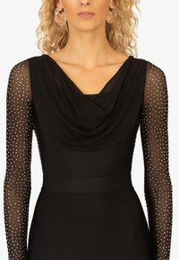 Schwarzes Kleid mit einem drapierten Ausschnitt, langen durchsichtigen Ärmeln, die mit silbernen Nieten verziert sind, und einem taillierten Oberteil mit glatter Textur.