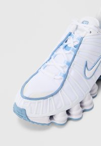 Hvit joggesko med lyseblå detaljer, mesh-overdel og særegen polstret såle med flere avrundede segmenter.