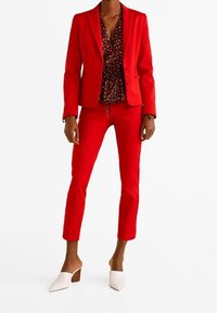 Punainen räätälöity bleiseri ja siihen sopivat kapealahkeiset housut, alla musta kukkakuvioinen paita. Valkoiset avokärkiset mules-kengät, joissa on neliskulmainen korko, täydentävät asun.