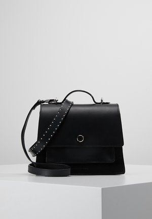 Bolso de mano de cuero negro con asa superior, solapa frontal, detalle de botón plateado y correa de hombro ajustable con tachuelas sobre superficie blanca.