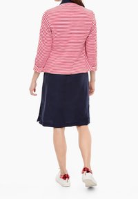 Rood-wit gestreepte jerseyjas met 3/4 mouwen, gedragen over een marineblauwe rok en gecombineerd met witte sneakers met rode accenten.