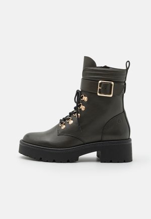 Bottine en cuir vert foncé avec quincaillerie dorée, devant à lacets, détail de boucle sur le côté et semelle épaisse noire à crampons.