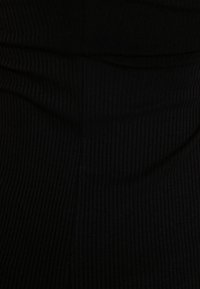Tissu ribbé noir avec une surface texturée ; présentant des lignes verticales et une finition lisse, mettant en avant la flexibilité et l'élasticité du tissu.