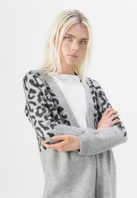 Cardigan grigio realizzato in morbido knitted, con stampa leopardata nera sulle maniche e corpo grigio uniforme. Design aperto sul frontale con polsini a coste.