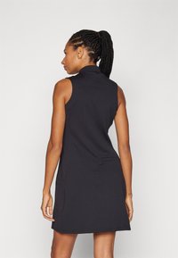 Μαύρο χωρίς μανίκια φόρεμα με ψηλό γιακά, με χαλαρή εφαρμογή και μικρή πίσω τσέπη, κατασκευασμένο από μαλακό, ελαστικό υλικό.