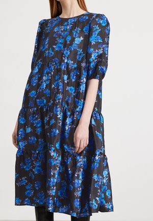 Czarna sukienka midi z falbanami w niebieski kwiatowy wzór, z bufiastymi, sięgającymi do łokcia rękawami i okrągłym dekoltem, noszona przez kobietę.