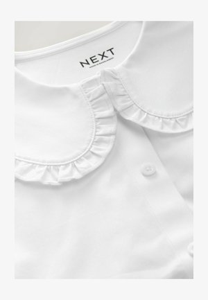 Bluză albă cu guler volan, închidere cu nasturi și textură de țesătură netedă. Eticheta brandului vizibilă în interiorul gulerului.