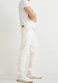 Jeans de mezclilla blanca con un corte recto y detalles mínimos. Presenta un parche de cuero y costuras sutiles. Combinados con zapatillas blancas.