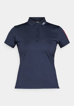 Granatowa koszulka polo wykonana z gładkiego materiału, z kołnierzykiem, zapięciem na trzy guziki oraz czerwonym tekstem na rękawie. Logo na kołnierzyku.