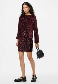 Completo in maglia bordeaux con paillettes e gonna abbinata, con maniche lunghe e superficie testurizzata, abbinato a scarpe nere con cinturino a T e una borsa piccola.