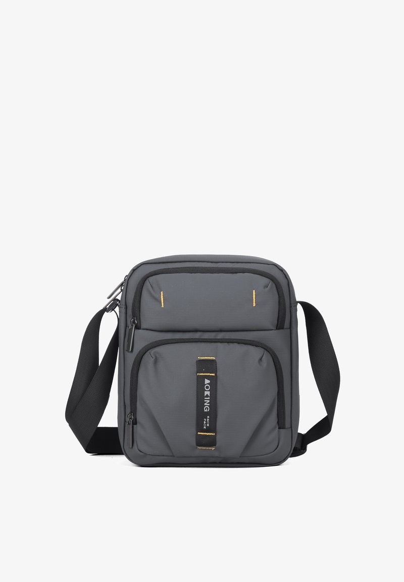 Borsa a tracolla grigia con superficie testurizzata, doppie tasche anteriori e cuciture gialle. Presenta una tracolla regolabile e una patch con il logo.