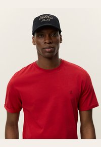 Rød bomull t-skjorte med rullede ermer og en marineblå caps med brodert tekst, som skaper et sporty og avslappet utseende.