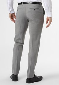 Graue Anzughose mit taillierter Passform, zwei Gesäßtaschen mit Knöpfen und glatter Stoffstruktur. Kombiniert mit schwarzen Schuhen.