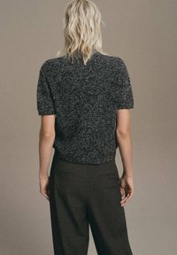 Texturovaný černobílý skvrnitý pletený top s krátkými rukávy, spárovaný s tmavými kostkovanými kalhotami. Zaměřeno na minimalistický design a čisté linie.