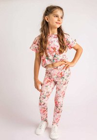 Różowy zestaw składający się z kwiecistej bluzki crop top i legginsów z zielonymi akcentami. Posiada wzór kwiatowy, krótkie rękawy i dopasowany krój. W zestawie białe trampki.