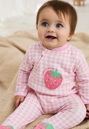 Baby trägt rosa-weiß karierten Schlafanzug mit lächelnden Erdbeer-Patches und sitzt auf einer beigen Decke.